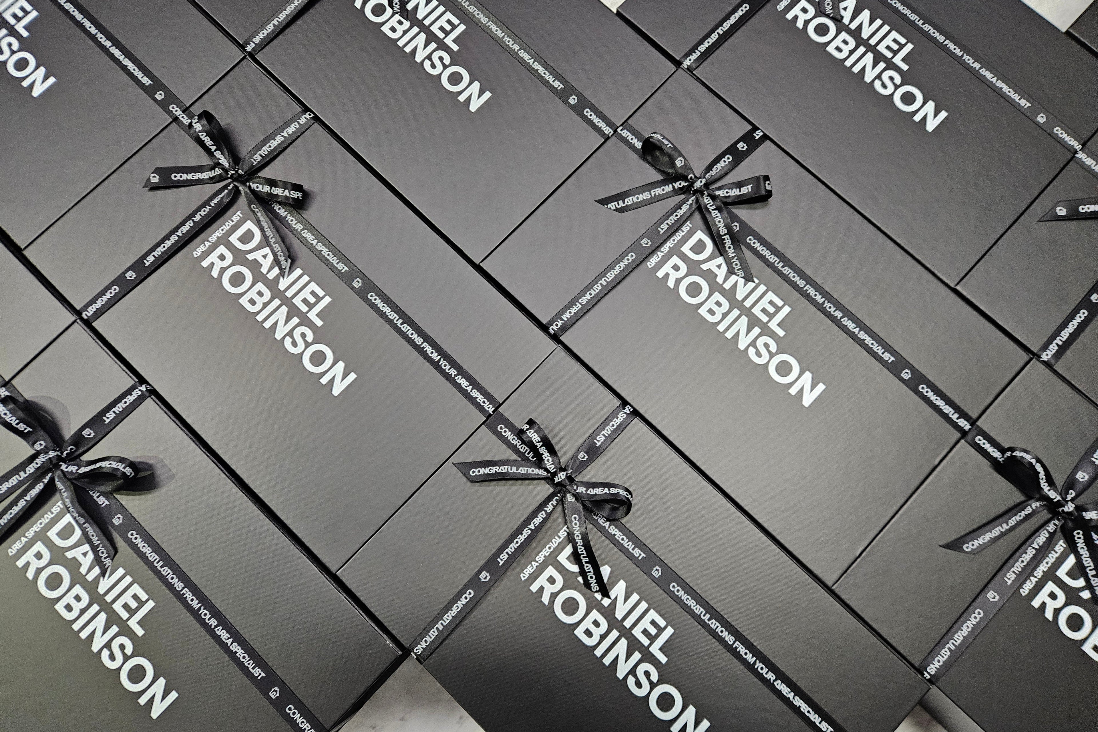 Multiple black 'Daniel Robinson' giftboxes with ribbons on a light background