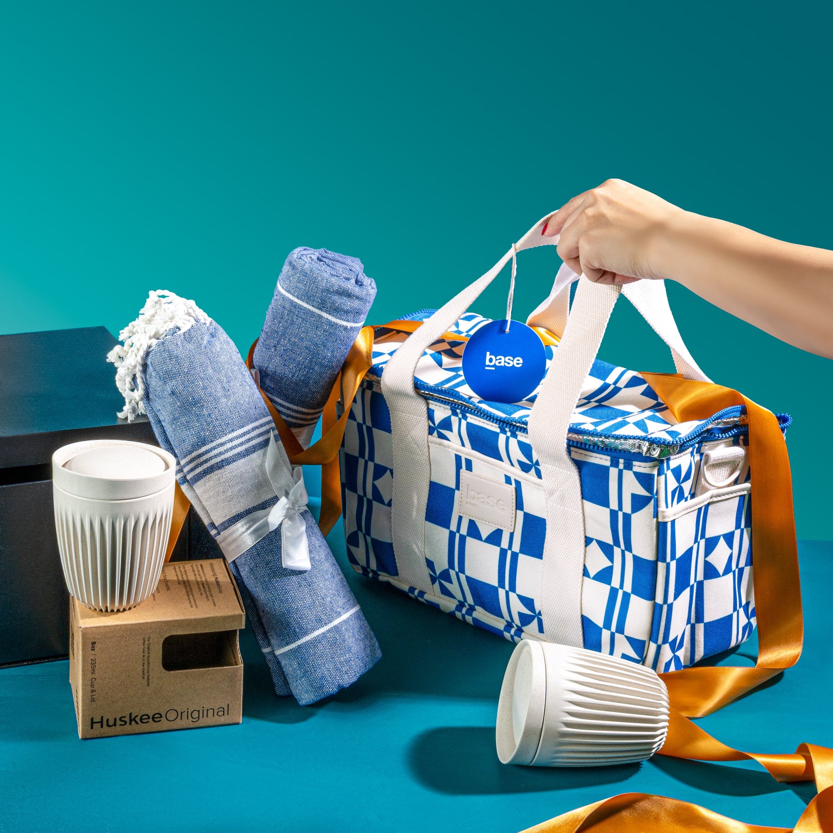 Blue and white patterned cooler bag with towels and two reusable cups on a teal background